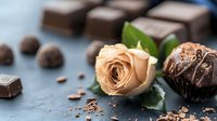 Elegant peach rose with dark chocolate pralines and truffles on dark stone background, romantic dessert composition with fresh flower and cocoa treats.