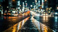 Blurred city street at night with wet asphalt reflecting colorful lights from traffic and buildings creating bokeh effect for urban transportation concepts.
