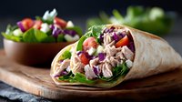 Fresh tuna salad wrap with mixed greens, tomatoes and purple cabbage on wooden board. Healthy lunch option for meal prep and quick dining.