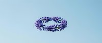 Purple floral wreath with delicate leaves and flowers arranged in circular frame on light blue background for wedding invitations and decorative designs.