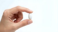 Hand holding white pill or medication tablet between fingers on clean background for healthcare and pharmaceutical concepts.