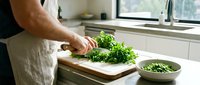 Man chopping fresh green herbs on wooden cutting board in modern kitchen preparing healthy meal ingredients for cooking.