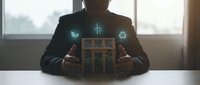 Businessman holding wooden house model with glowing green energy icons representing sustainable development, renewable power, and eco-friendly building solutions for corporate responsibility.
