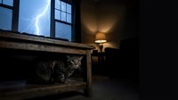 A tabby cat shelters under a wooden table during a thunderstorm, with lightning visible through a window and a warm lamp glowing overhead.
