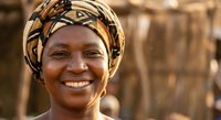 Smiling African woman wearing traditional colorful headwrap outdoors with warm natural lighting and blurred background for cultural diversity content.