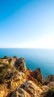 Scenic coastal cliff landscape with turquoise sea and rocky outcrop under clear blue sky, suitable for travel, nature, and tourism marketing materials.