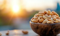 Fresh raw peanuts in rustic wooden bowl with warm golden sunlight creating beautiful bokeh background for healthy snacking and cooking ingredients.