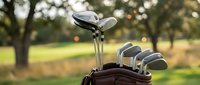 Golf clubs in leather bag on course with blurred trees and warm sunlight creating bokeh effect. Sports equipment ready for game on green fairway.