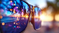 Tropical sunset beach scene reflected in stylish sunglasses lens with palm trees silhouette and colorful bokeh lights creating dreamy summer vacation mood.