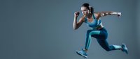 Athletic woman in blue sportswear jumping mid-air against gray background, demonstrating fitness, exercise, and dynamic movement for health and wellness content.