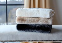 Stack of folded soft faux fur blankets in white, beige and black colors on window sill, cozy home textile arrangement for interior design and comfort.