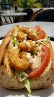 Crispy fried shrimp po boy sandwich with fresh lettuce, tomato and creamy sauce on crusty bread served at outdoor restaurant patio for lunch dining experience.