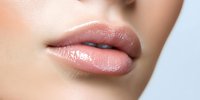 Close up of plump, glossy natural pink lips on light skin tone female face showing professional makeup and skincare results against soft focus background.