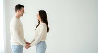 Young couple holding hands in matching cream sweaters and jeans against white background for relationship and love concepts in lifestyle photography.