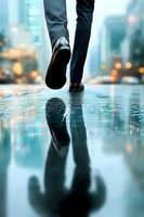 Business person walking on wet city street with reflection in puddle during rainy evening, dramatic perspective with bokeh lights in background.
