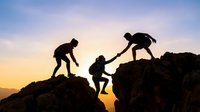 Team of hikers helping each other climb rocky mountain peak during golden sunset, silhouetted against colorful sky for teamwork and adventure concepts.
