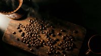 Roasted coffee beans scattered on rustic wooden cutting board with warm lighting creating cozy cafe atmosphere for beverage and food photography.