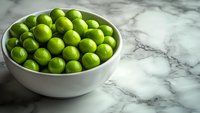 Fresh green limes in white ceramic bowl on marble countertop background with dramatic side lighting and copy space, food photography for healthy recipes.