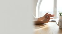 Woman hands typing on smartphone at wooden desk near window with natural sunlight for communication and technology concepts.