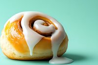 Glazed cinnamon roll with white icing dripping down on mint green background. Fresh baked pastry dessert for bakery menu and food advertising.