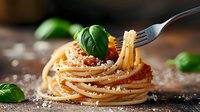Twirled spaghetti pasta with tomato sauce and fresh basil leaves on rustic wooden background, garnished with grated parmesan cheese and fork lifting noodles.