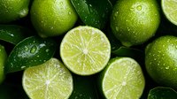 Fresh juicy limes with water drops and green leaves, close up view. Whole and sliced citrus fruits arranged on dark background for cocktails and cooking.