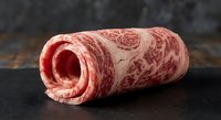 Premium marbled raw beef roll on dark slate surface showcasing rich fat distribution and meat texture for culinary and food photography applications.