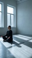 Young woman practicing meditation in minimalist room with natural light streaming through windows creating peaceful atmosphere for mindfulness and wellness.