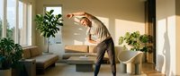Mature Caucasian man stretching at home in a bright modern living room surrounded by plants, enjoying a morning fitness routine.