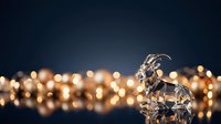 Crystal goat figurine standing against blurred golden bokeh lights on dark background, suitable for luxury, success, and festive holiday designs.