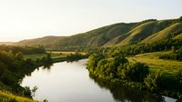 Scenic river flowing through lush green valley with rolling hills at golden hour, suitable for travel, nature, and landscape design projects.