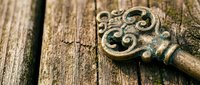 Ornate vintage brass key with decorative scrollwork lying on weathered wooden surface with natural cracks and moss details for antique design projects.