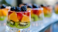 Fresh layered fruit dessert with blackberries, mango, strawberries and kiwi in individual glass portions, topped with cream and berries for catering events.