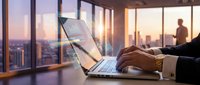 Professional businessman working on laptop in modern office with city skyline view during golden hour sunset, corporate workspace productivity concept.