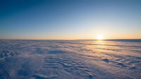 Frozen landscape with golden sunrise over snow-covered terrain, featuring rippled ice patterns and clear sky. Suitable for winter backgrounds, nature themes, and seasonal designs.