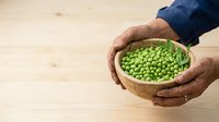 Farmer's hands holding wooden bowl filled with fresh green peas on wooden surface for agriculture and food production concepts.