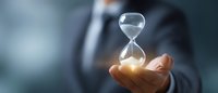 Businessman in dark suit holding glowing hourglass against blurred background, symbolizing time management and business deadline concept.