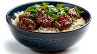 Asian meatballs with noodles in dark ceramic bowl garnished with fresh herbs and sesame seeds for restaurant menu and food photography.