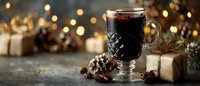 Festive glass of mulled wine with spices, pine cones, and wrapped gifts against blurred golden bokeh lights for holiday celebration.