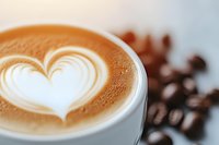 Creamy latte art heart pattern in white ceramic cup with roasted coffee beans scattered in background, shallow depth of field creates soft ambiance.