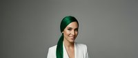 Confident young Caucasian woman with long green hair in white blazer smiling against gray background, bold style and modern beauty concept.