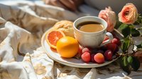 Morning tea setting with fresh grapefruit, orange, red grapes and pink ranunculus flower on ceramic plate with white linen tablecloth in natural light.