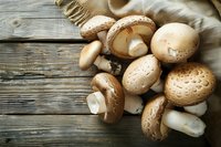 Fresh brown champignon mushrooms scattered on rustic wooden table with natural light, raw organic produce for cooking healthy meals.