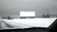 Blank billboard along a snowy highway seen through a car windshield in a winter storm, black and white, copy space for advertising.