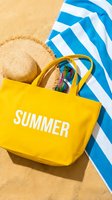 Yellow summer tote bag with straw hat and sunglasses on sandy beach beside blue striped towel, vibrant vacation flatlay for seasonal promotions.