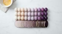 Gradient ombre eggs arranged in rows from cream to purple with wooden discs on marble surface for Easter spring decoration crafts.