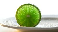 Sliced lime with translucent green flesh on white plate, isolated on white background. Fresh citrus fruit for beverage, cooking, and food styling projects.