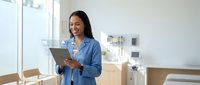 Young Asian businesswoman using digital tablet in modern office space with natural lighting and minimalist design for professional workflow.
