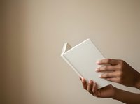 A person with medium brown skin tone holds an open blank white book against a neutral beige background, suitable for publishing, education, and reading concepts.