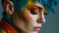 Young woman with vibrant blue hair and artistic golden glitter makeup on face and eyelids, creative beauty portrait for fashion and cosmetic projects.